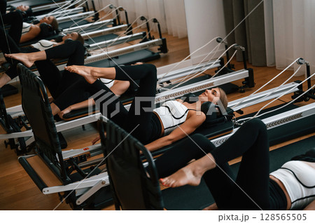 Lying down in a row and doing stretches. Women in fitness center are doing exercises Lying down in a row and doing stretches. Women in fitness center are doing exercises 128565505