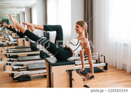 Sitting on the special chair. Young woman in fitness center is doing exercises Sitting on the special chair. Young woman in fitness center is doing exercises 128565524