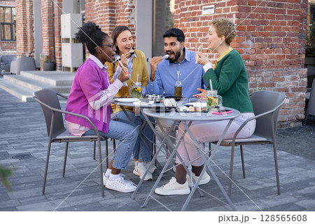 Friends enjoying sushi and drinks at an outdoor restaurant. They are eating and laughing together. Friends enjoying sushi and drinks at an outdoor restaurant. They are eating and laughing together. 128565608
