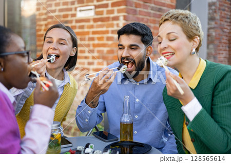 A diverse group of friends enjoys a sushi meal together, savoring the flavors and company outdoors. 128565614