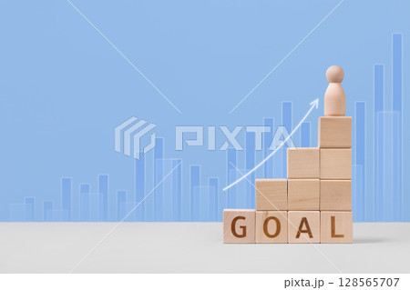 Wooden cubes with the words goal, white arrow and wooden man are a symbol of success, business progress, strategic development of a company, startup. Business concept Wooden cubes with the words goal, white arrow and wooden man are a symbol of success, business progress, strategic development of a company, startup. Business concept 128565707