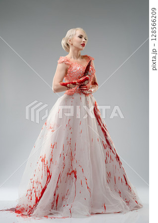 Bride in blood-stained gown striking a powerful pose in studio setting 128566209