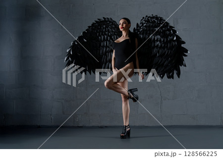 Woman wearing lingerie with black wings poses confidently in a studio setting 128566225