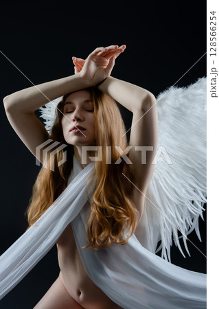 Red naked woman with angel wings posing gracefully in a studio setting 128566254