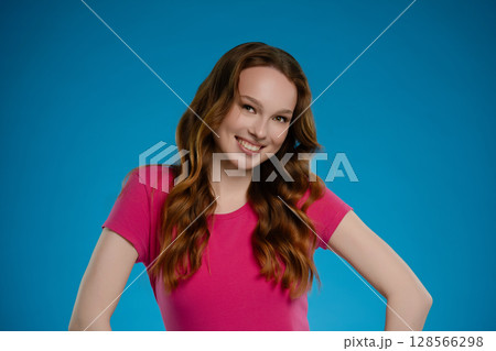 Woman posing in a studio environment, expressing joy and confidence with a vibrant blue backdrop 128566298