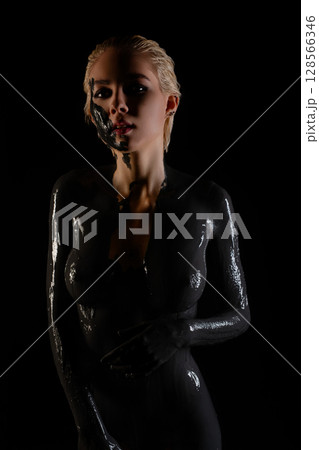 A woman stands confidently, her body adorned with glossy paint and tattoos 128566346