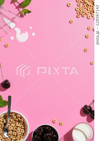 Vertical banner with cereal rings, cherries, mint leaves, a spoon, spilled milk, and a bowl on pink background. A breakfast concept with space for your text. 128567142