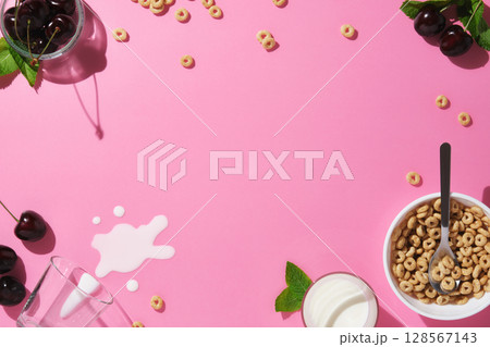 Frame with cereal rings, cherries, mint leaves, a spoon, spilled milk, and a bowl on pink background. Breakfast concept with space for your text. 128567143