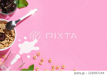 Pink breakfast background with cereal rings, cherries, mint leaves, a spoon, spilled milk, and a bowl. Space for your text. 128567144