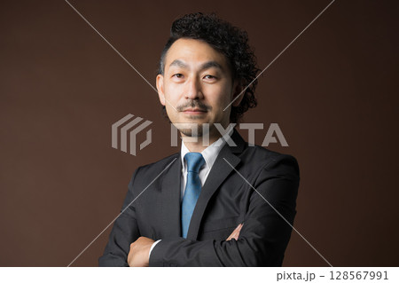 茶色背景でスーツを着た腕を組む笑顔のビジネスマン　信頼や信用のイメージ　カメラ目線 128567991