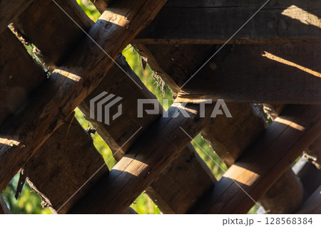 Rustic wooden roof lattice illuminated by sunlight, casting intricate shadows 128568384