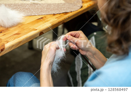 Woman's hands felting wool on wooden table surface in artisan workshop 128568497