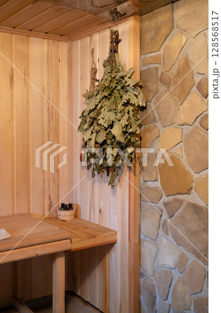 Cozy wooden sauna interior with birch leaves and stone wall Cozy wooden sauna interior with birch leaves and stone wall 128568517
