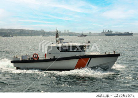 A sleek boat glides swiftly past a distant city skyline A sleek boat glides swiftly past a distant city skyline 128568675