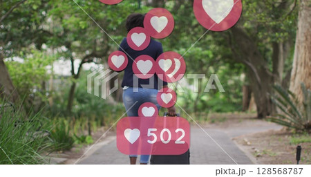 Image of social media heart icons over african american woman riding bicycle in park Image of social media heart icons over african american woman riding bicycle in park 128568787