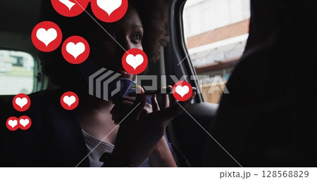Image of social media heart icons over african american woman with face mask using phone in car 128568829