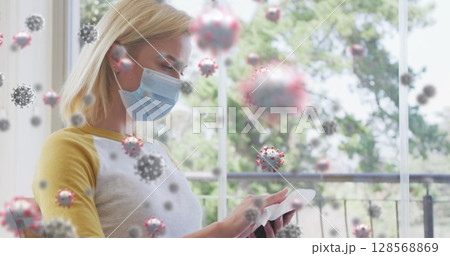 Image of covid 19 cells over caucasian blonde woman wearing face mask using smartphone Image of covid 19 cells over caucasian blonde woman wearing face mask using smartphone 128568869