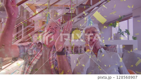 Happy caucasian senior couple in party hats making birthday image call, with gold confetti 128568907