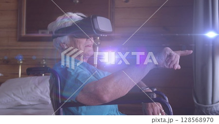 Image of light and lens flare over smiling senior caucasian woman in wheelchair using vr headset 128568970