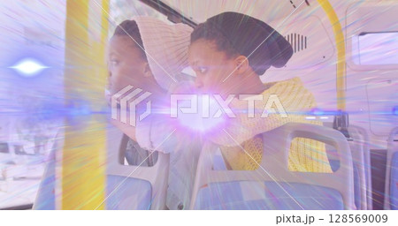 Image of light beam and lens flare over two african american woman on bus looking out of window 128569009