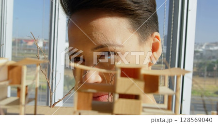Image of pink and blue light beams flaring over female architect looking at architectural model 128569040