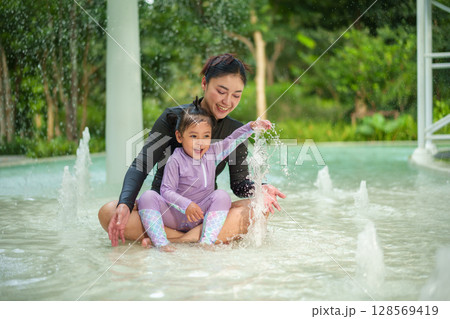 happy mother with toddler girl playing water splashing in swimming pool 128569419