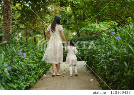 mother and toddler girl in white dress walking in flower garden mother and toddler girl in white dress walking in flower garden 128569428