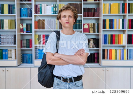 Portrait of handsome confident serious teenage boy looking at camera in library 128569693