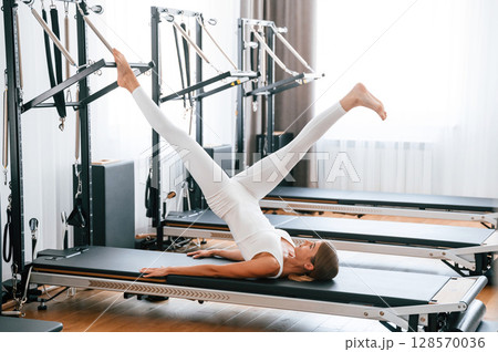 Lying down and stretching legs. Young woman in fitness center is doing exercises Lying down and stretching legs. Young woman in fitness center is doing exercises 128570036