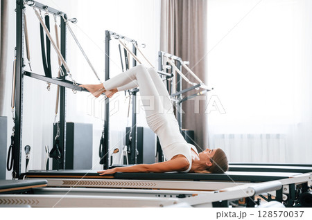 Lying down and stretching legs. Young woman in fitness center is doing exercises 128570037