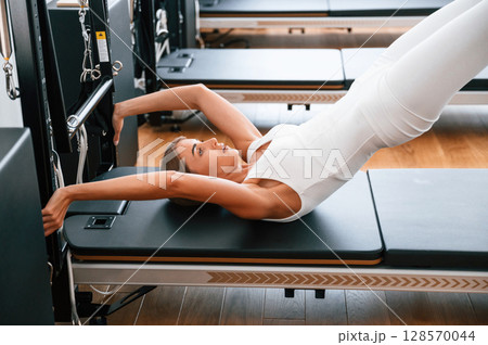 In white sportive clothes. Young woman in fitness center is doing exercises In white sportive clothes. Young woman in fitness center is doing exercises 128570044