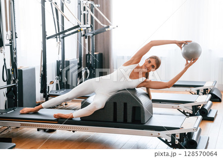 Holding ball in hands. Young woman in fitness center is doing exercises 128570064