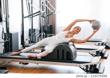 Holding ball in hands. Young woman in fitness center is doing exercises Holding ball in hands. Young woman in fitness center is doing exercises 128570066