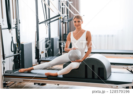 Holding ball in hands. Young woman in fitness center is doing exercises 128570196