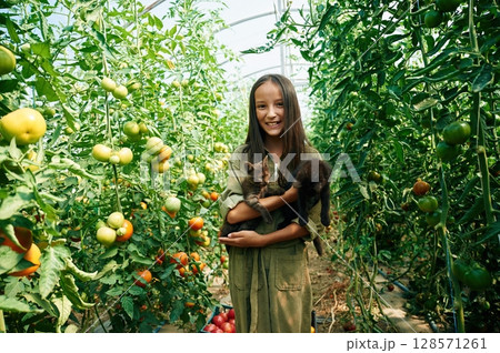 Black cats are in hands. Little girl is in the garden with tomatoes Black cats are in hands. Little girl is in the garden with tomatoes 128571261