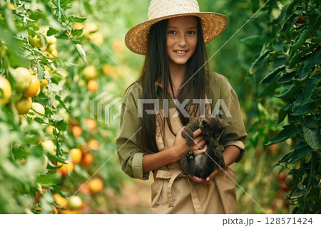 Holding cute kitten in hands. Little girl is in the garden with tomatoes 128571424