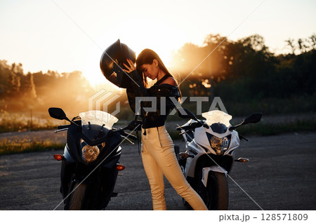 Wearing the protective helmet. Woman is with motorcycle outdoors 128571809