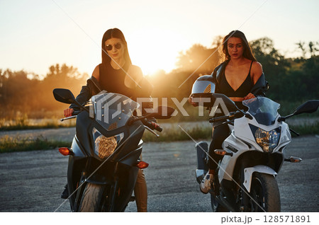 Front view. Two women on motorcycles are together outdoors Front view. Two women on motorcycles are together outdoors 128571891