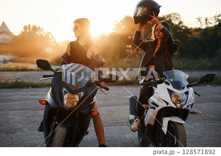 Front view. Two women on motorcycles are together outdoors 128571892