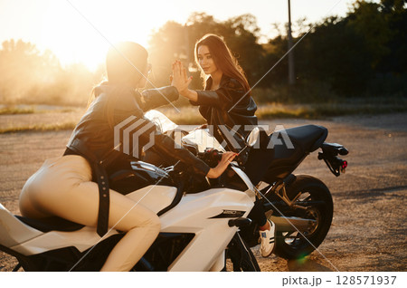High five gesture. Two women on motorcycles are together outdoors 128571937