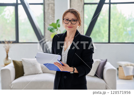 Portrait of woman mentor teacher counselor with clipboard in office looking at camera 128571956