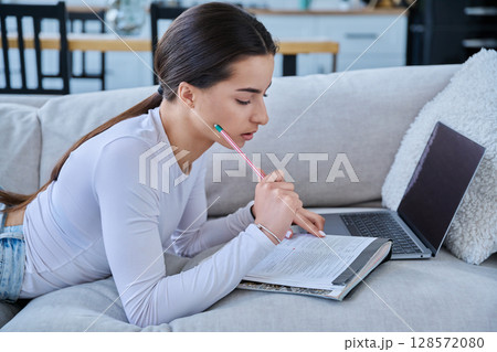 Young student girl study online, lying at home on couch with laptop, notebook 128572080