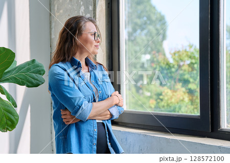 Middle aged calm beautiful woman looking out window Middle aged calm beautiful woman looking out window 128572100