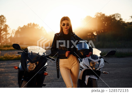 Holding protective helmet in hand. Woman is with motorcycle outdoors Holding protective helmet in hand. Woman is with motorcycle outdoors 128572135