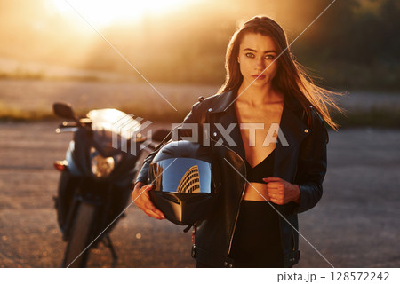 Standing and posing. Woman is with motorcycle outdoors Standing and posing. Woman is with motorcycle outdoors 128572242