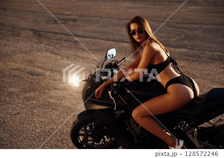 Side view, sitting. Hot woman in underwear is with motorcycle outdoors 128572246