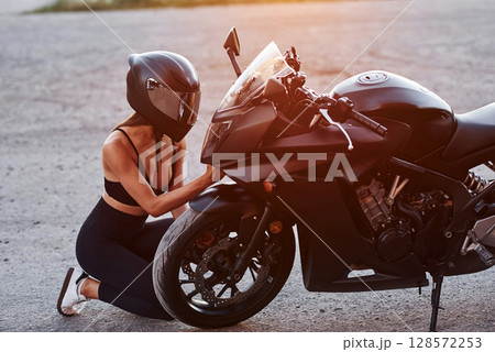 Sitting, taking care of front view. Woman is with motorcycle outdoors Sitting, taking care of front view. Woman is with motorcycle outdoors 128572253