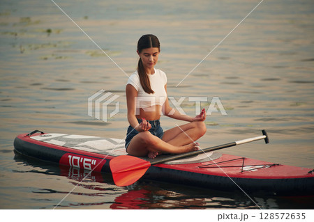 Sitting in lotus pose. Young woman is on sup boards in the lake Sitting in lotus pose. Young woman is on sup boards in the lake 128572635