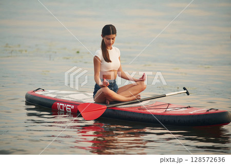Sitting in lotus pose. Young woman is on sup boards in the lake Sitting in lotus pose. Young woman is on sup boards in the lake 128572636