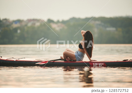 Aginst background with trees far away. Young woman is on sup boards in the lake Aginst background with trees far away. Young woman is on sup boards in the lake 128572752